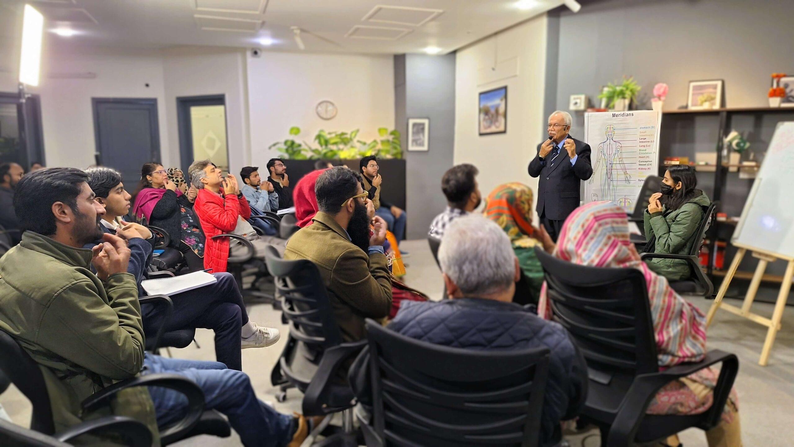 A group of people practice omw energy tapping with dr imtiaz mehmud in a group healing session